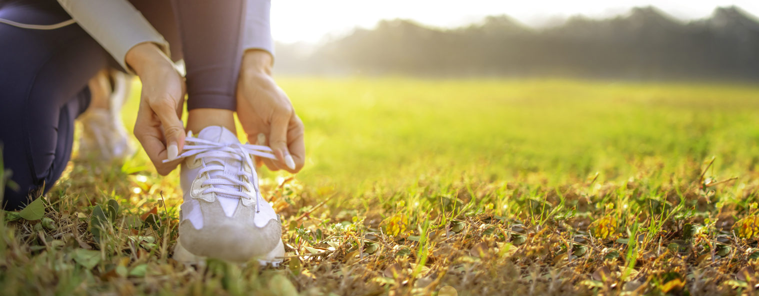 Close up stock image of a woman kneeling in a field and tying her brown and white sneaker